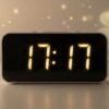 薄暗い部屋で、デジタル時計の「17:17」の表示が金色に光り、背景には幸運を象徴する四つ葉のクローバーの影が浮かび上がっている画像
